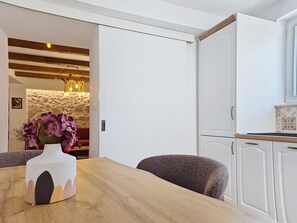 A dining area with a wooden table and chairs, a vase with flowers, and a kitchen with white cabinets. - Blazov dvor by Interhome (Zaton)