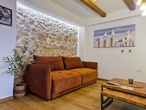 A room with a stone wall, a brown sofa, a wooden coffee table, and a painting of seagulls. - Blazov dvor by Interhome (Zaton)