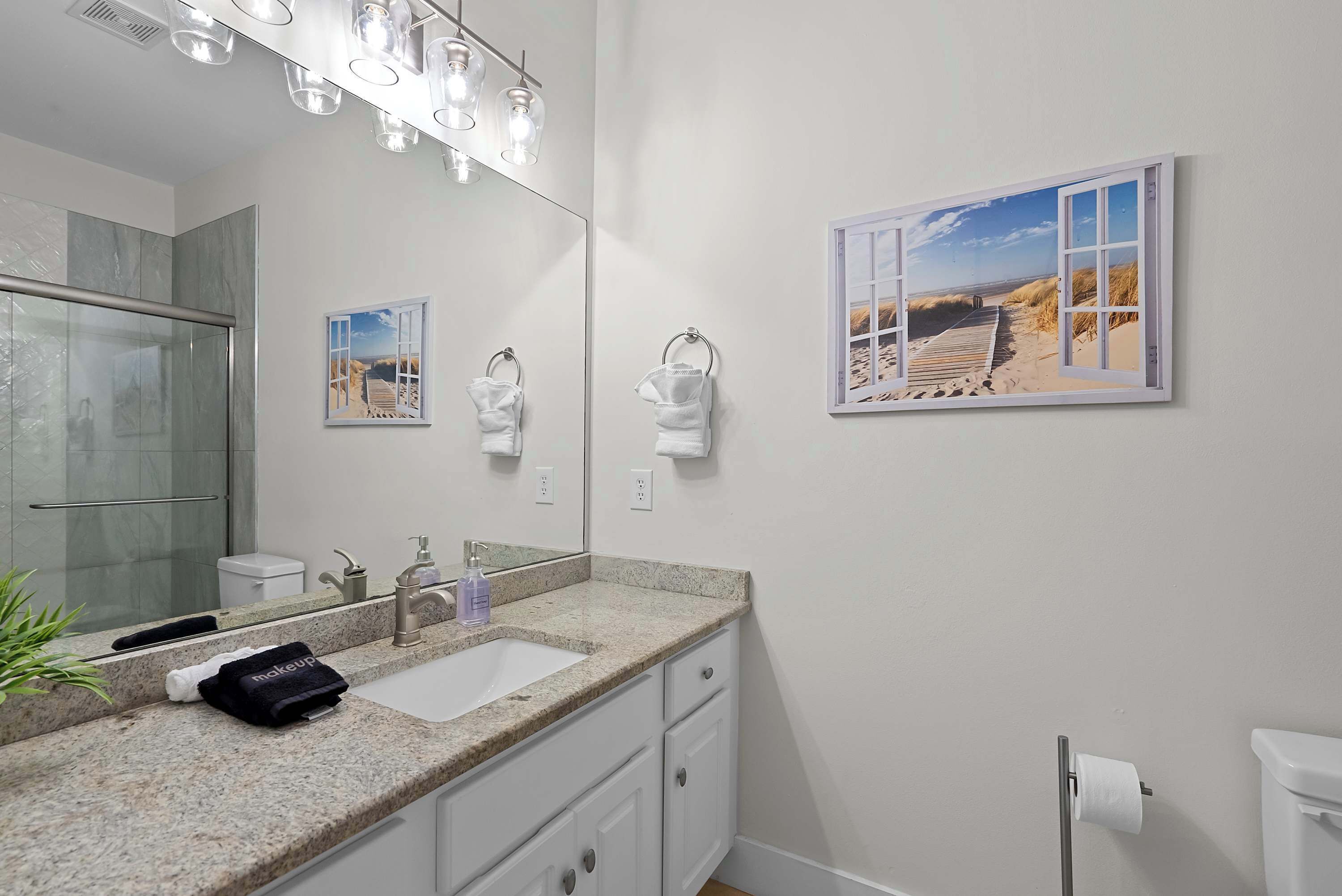 A bathroom with a large mirror, a sink, a towel rack, and a window with a beach view.