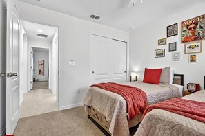 Ein Schlafzimmer mit zwei Betten, einer Tür zu einem anderen Raum und einer Wand mit gerahmten Bildern.