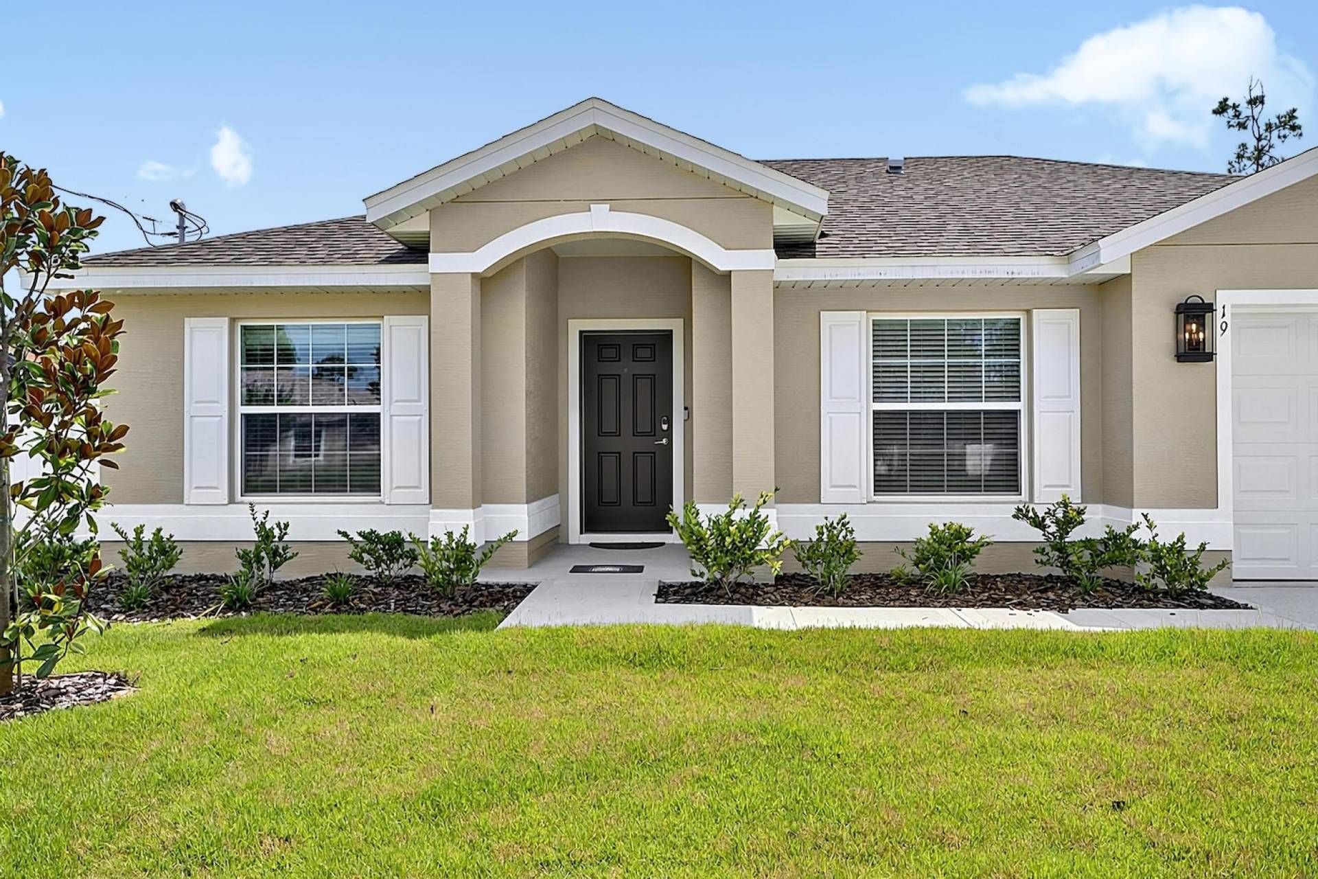 A single-story house with a front entrance, two windows with shutters, a garage door, and a well-maintained lawn.