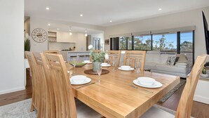 Un coin repas avec une table en bois, dressée pour quatre personnes et entourée de chaises, dans une cuisine moderne dotée d’une grande fenêtre.
