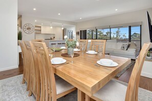 Un coin repas avec une table en bois, dressée pour quatre personnes et entourée de chaises, dans une cuisine moderne dotée d’une grande fenêtre.