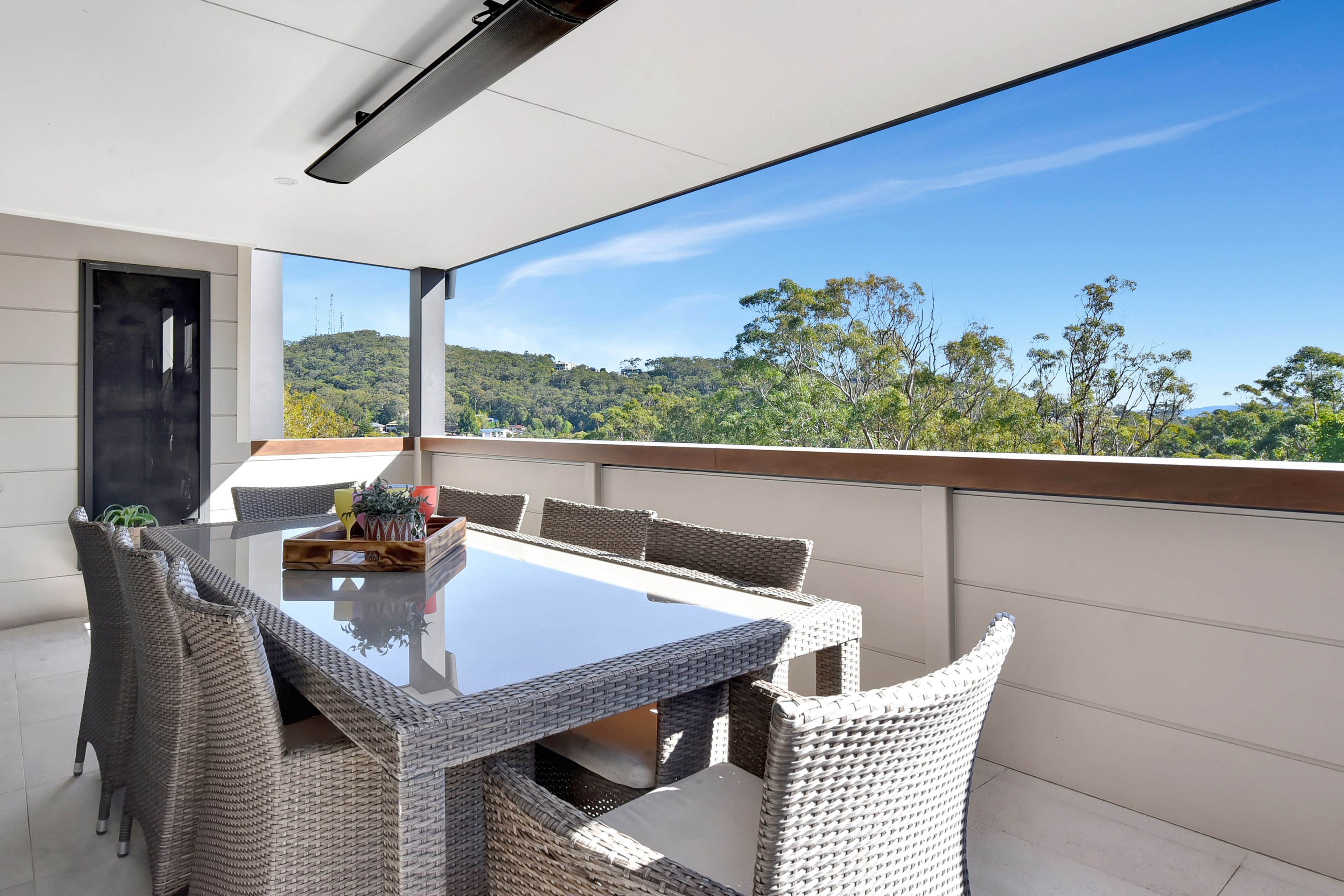 A balcony with a glass table and wicker chairs, overlooking a forested landscape.