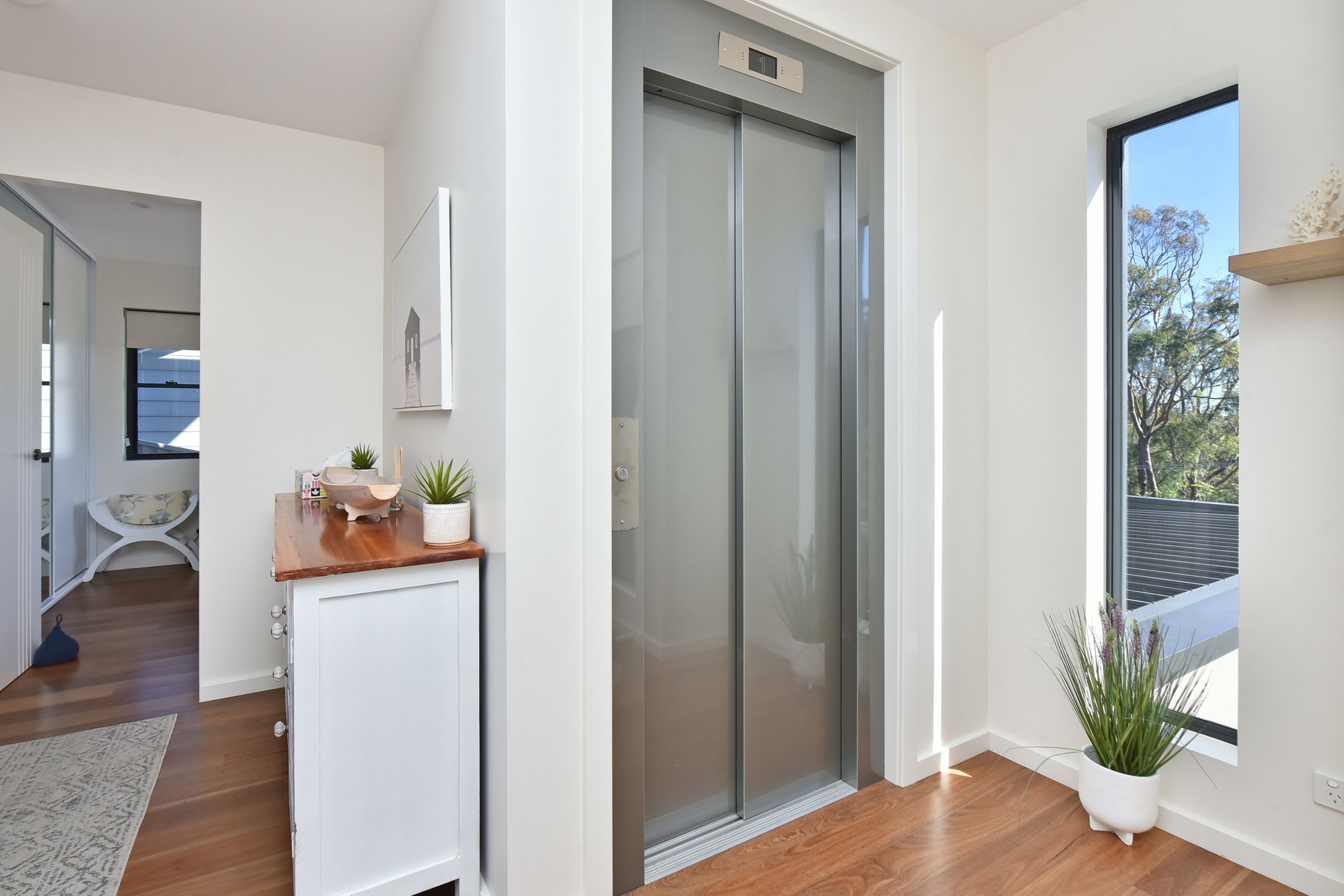 A modern interior with a sliding door, a small white cabinet, a wooden counter, and a potted plant.