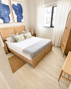 A neatly arranged bedroom with a wooden bed, a bedside table, a lamp, and a window with curtains. - Luxury 1BR Condo w/ Private Picuzzi • 6 Min to Beach • Sleeps 4 (Punta Cana)