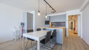 A modern kitchen with a central island, white dining table with chairs, and a visible fire extinguisher. - 8th-floor apartment with sea view (Middelkerke)