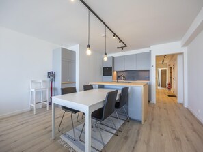 Eine moderne Küche mit einer zentralen Kochinsel, einem weißen Esstisch mit Stühlen und einem sichtbaren Feuerlöscher.