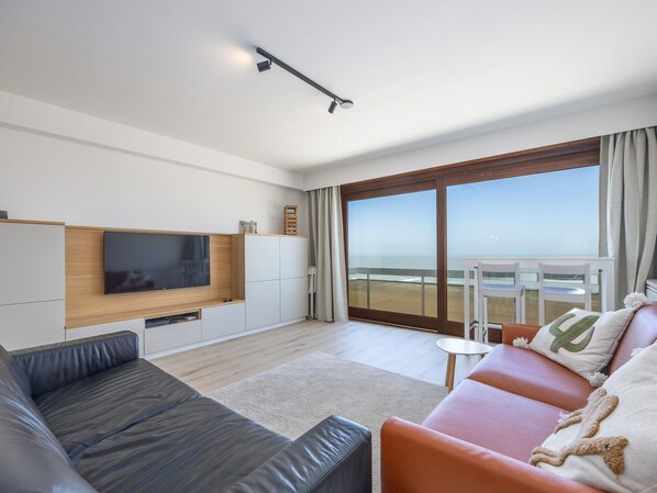 Una sala de estar moderna con un televisor de pantalla plana, sofás de cuero, una mesita y un balcón con vistas.