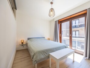 Un dormitorio con cama, lámparas de noche, ventana con cortinas y una lámpara en el techo.