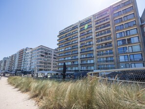 Fila de edificios residenciales altos con balcones, un camino de arena y una valla.
