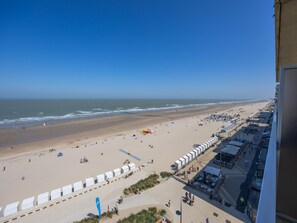 Blick auf einen Strand von einem erhöhten Aussichtspunkt aus, inklusive einer Uferpromenade mit Geschäften und blauem Himmel.