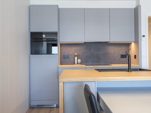 Eine moderne Küche mit grauen Schränken, einer Holz Arbeitsplatte, einem eingebauten Backofen und einem Edelstahl-Wasserhahn.