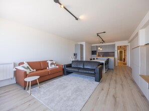 Una sala moderna con un sofá, una mesa de centro y una alfombra. Hay una zona de cocina con una mesa y sillas.