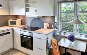 Eine moderne Küche mit integriertem Mikrowellenherd, Backofen und Grill, ein Fenster mit Blick auf Grünflächen und ein kleiner Tisch mit Blumen in einer Vase.