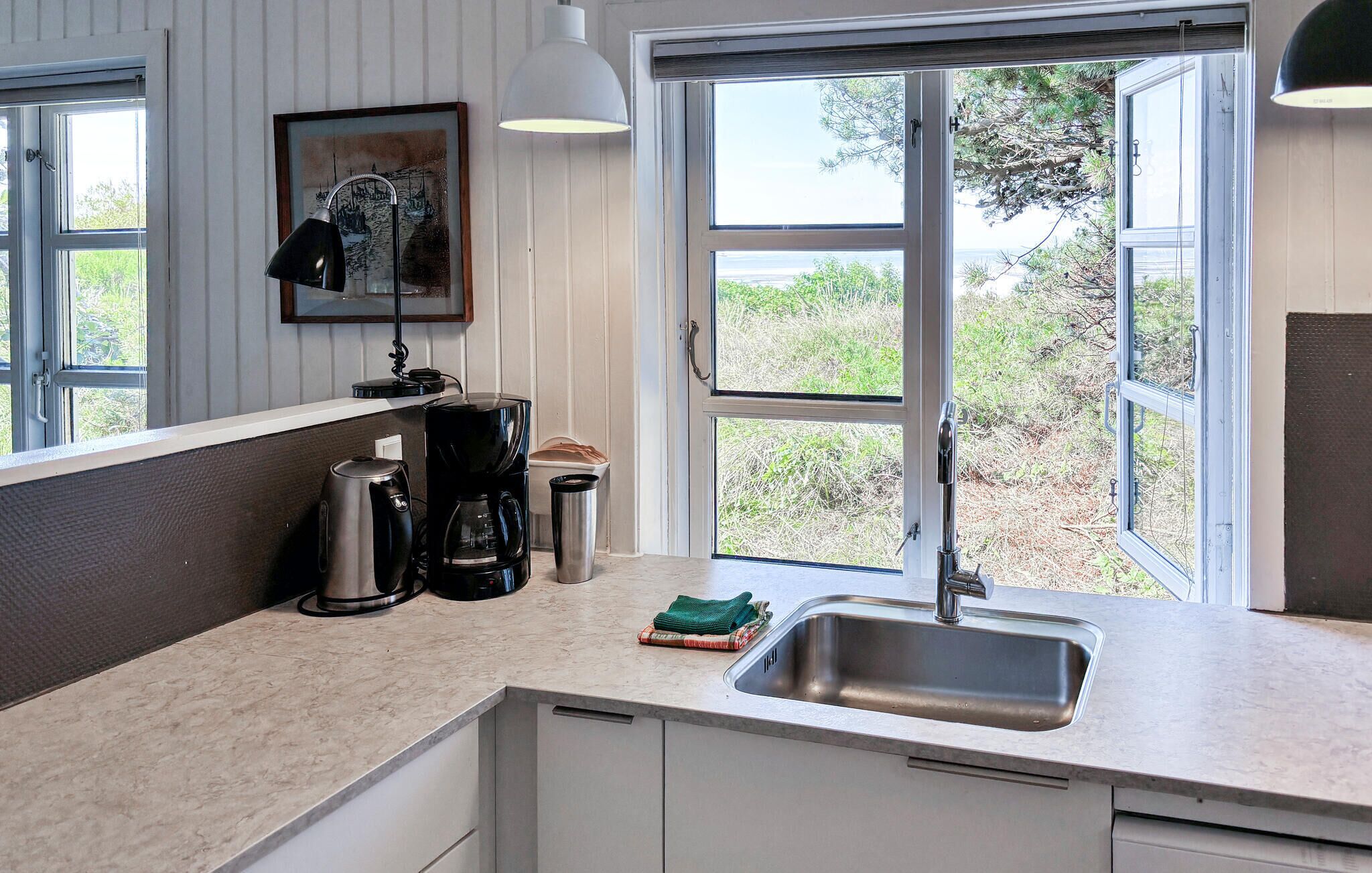 Una cocina con un lavamanos, una cafetera y un cuadro en la pared.