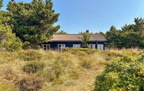 Ein Haus mit rotem Ziegeldach, umgeben von üppigem Grün und hohem Gras.