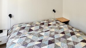 Ein Einzelbett mit Patchwork-Decke, ein Nachttisch und eine Wandlampe.