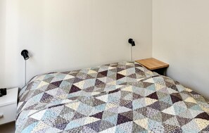 Ein Einzelbett mit Patchwork-Decke, ein Nachttisch und eine Wandlampe.