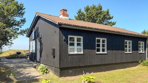Ein dunkles Holzhaus mit Ziegeldach, Schornstein und gepflasterter Auffahrt.