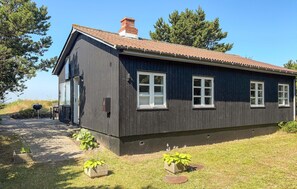 Ein dunkles Holzhaus mit Ziegeldach, Schornstein und gepflasterter Auffahrt.