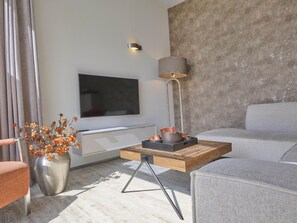 A modern living room with a flat-screen TV, a lamp, and a coffee table with decorative items. - Beach lodge on the beach (Callantsoog)