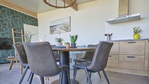 Un comedor moderno con una mesa redonda, cuatro sillas grises tapizadas y una lámpara colgante central.