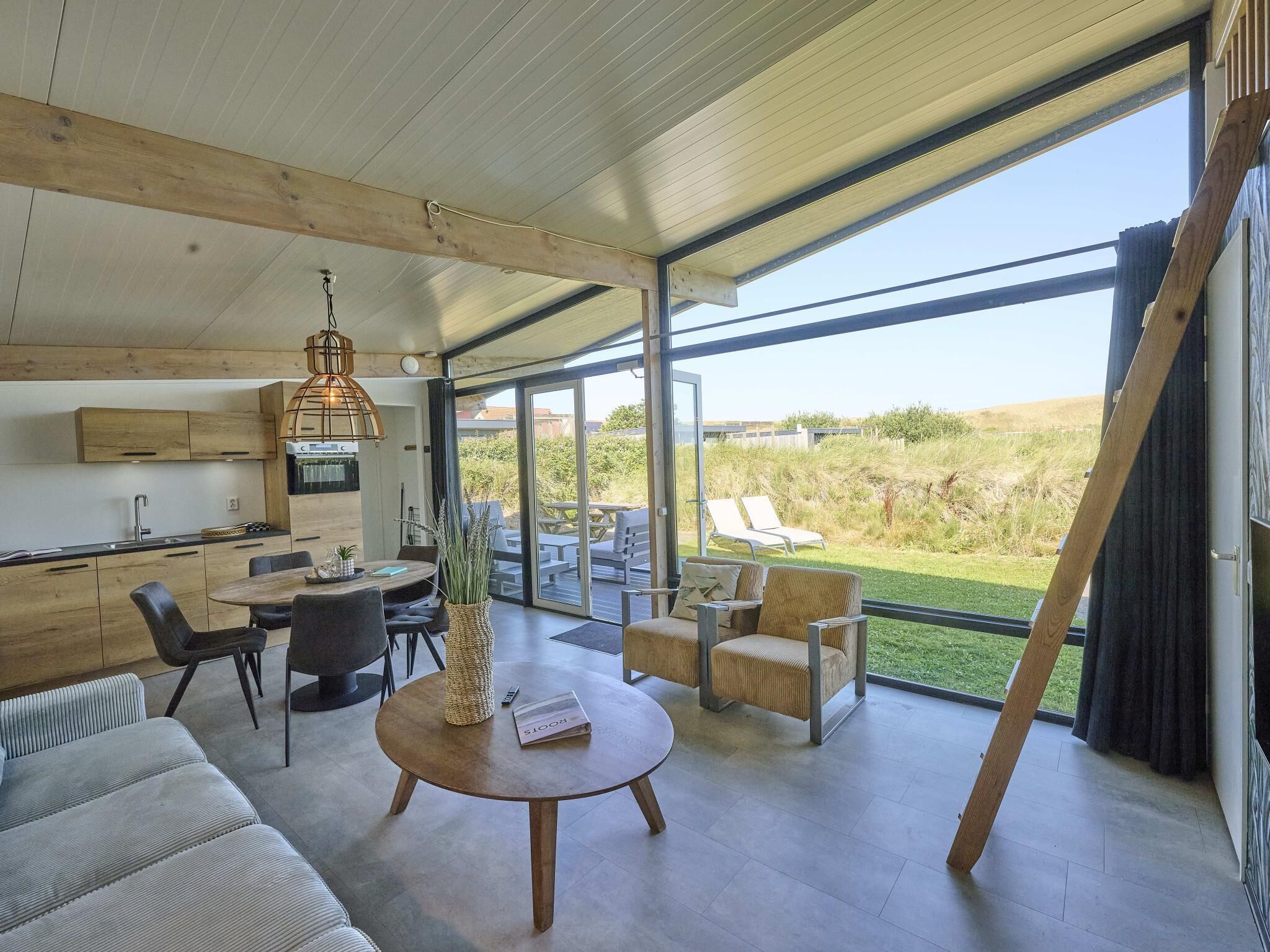 Eine moderne Küche mit Holzausstattung und einem eingebauten Backofen, ein Essbereich mit rundem Tisch und Stühlen sowie eine große Schiebetür zu einer Terrasse im Freien mit Blick auf die Landschaft.