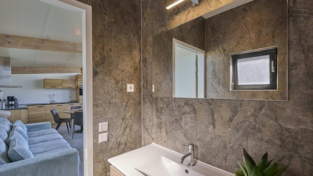 Un baño moderno con un espejo grande, un lavabo blanco y una planta en maceta.