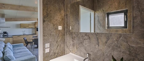 A modern bathroom with a large mirror, a white sink, and a potted plant.