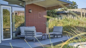 Un espacio exterior moderno con área de descanso, puerta de vidrio, pared de listones de madera y estructura de techo plano.