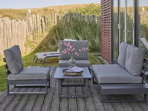 An outdoor seating area with a sofa and chairs, a table with a vase of flowers, and a book titled 'ROOTS'. - Luxury beach lodge by the beach. (Callantsoog)