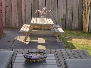 A wooden picnic table with benches, a glass vase with pink flowers, and a basket with a label on a wooden deck. - Luxury beach lodge by the beach. (Callantsoog)