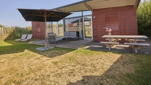 Uma área de estar ao ar livre moderna, com um terraço coberto, deck de madeira e mesa para piquenique.