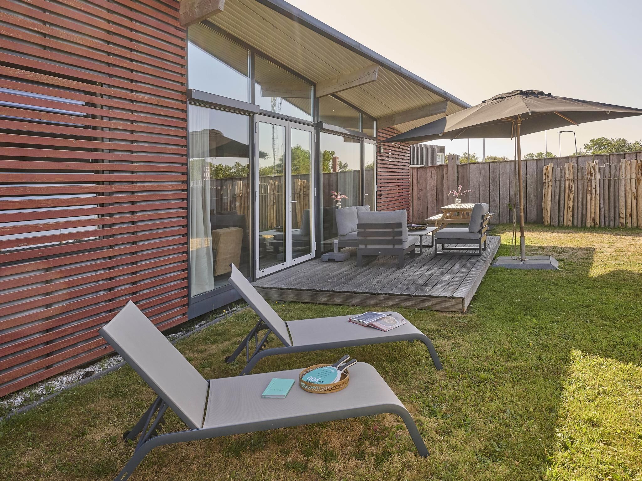 Un patio moderno al aire libre con terraza de madera, un área de estar cubierta y un ventanal que da a una habitación.