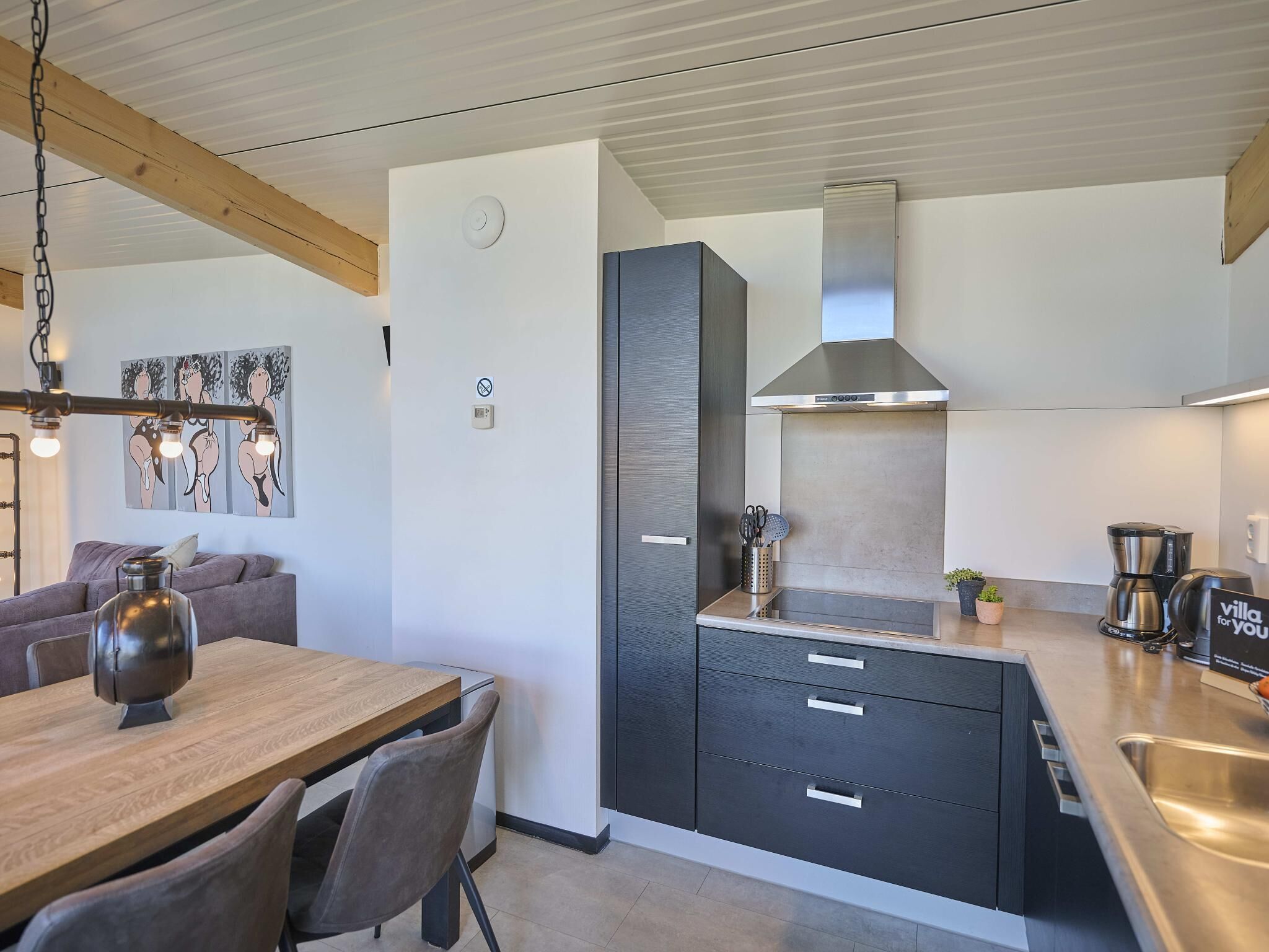 A modern kitchen with a wooden ceiling, a built-in stove, and a coffee maker on the counter.
