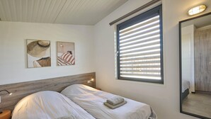 Quarto com duas camas, cabeceira de madeira, uma janela grande com persianas e obras de arte na parede.