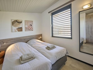 Ein Schlafzimmer mit zwei Betten, einem Holz-Kopfteil, einem großen Fenster mit Jalousien und Bildern an der Wand.