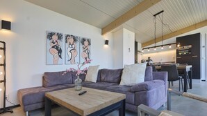 Uma sala de estar moderna com um sofá, uma mesa de centro e um vaso de flores. Cozinha e área de jantar visíveis ao fundo.