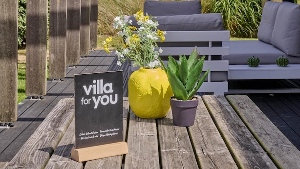 A wooden deck with a sign reading 'villa for you,' a yellow vase with flowers, and a potted plant. - Holiday home 350 meters from the beach (Callantsoog)