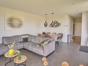 Una sala de estar moderna con un sofá modular gris, una mesa de comedor con sillas, lámparas colgantes y un elemento decorativo en la pared.