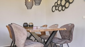 A dining area with a wooden table and chairs, a decorative wall piece, and a hanging light fixture. - Holiday home 350 meters from the beach (Callantsoog)