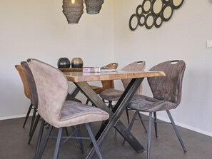 A dining area with a wooden table and chairs, a decorative wall piece, and a hanging light fixture. - Holiday home 350 meters from the beach (Callantsoog)