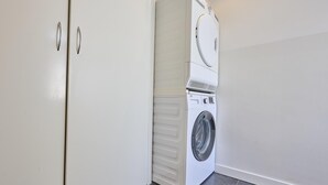 A laundry room with a stacked washer and dryer, a white door, and grey tiled flooring. - Delightful detached beach villa (Callantsoog)