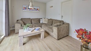 A living room with a sofa set, a coffee table with a plant and magazine, a painting on the wall, and a door. - Delightful detached beach villa (Callantsoog)