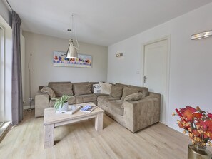 Ein Wohnzimmer mit einer Sofagarnitur, einem Couchtisch mit Pflanze und Zeitschrift, einem Bild an der Wand und einer Tür.