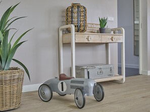 Ein altes Spielzeugauto, eine Korbpflanze und ein Holzregal mit einem Koffer und einem Willkommensschild.