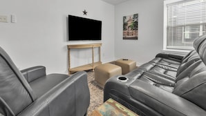 Un salón con televisor de pantalla plana, decoración con estrellas, un cuadro enmarcado y una ventana con persianas.