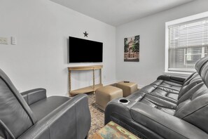 Een woonkamer met een flatscreen televisie, een steroverslag, een lijst met afbeelding en een raam met zonwering.