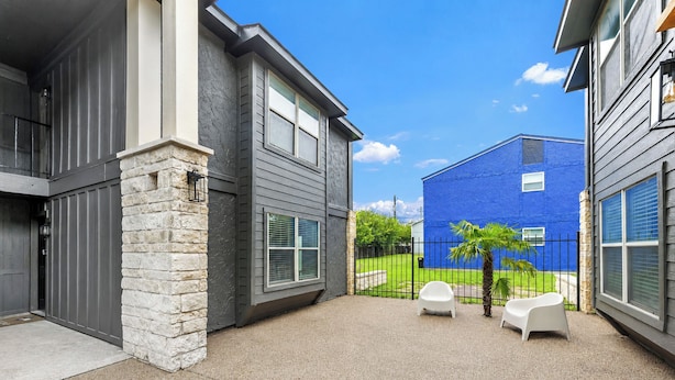 Un edificio residencial con fachada de piedra, un edificio azul al fondo y un patio con dos sillas blancas.